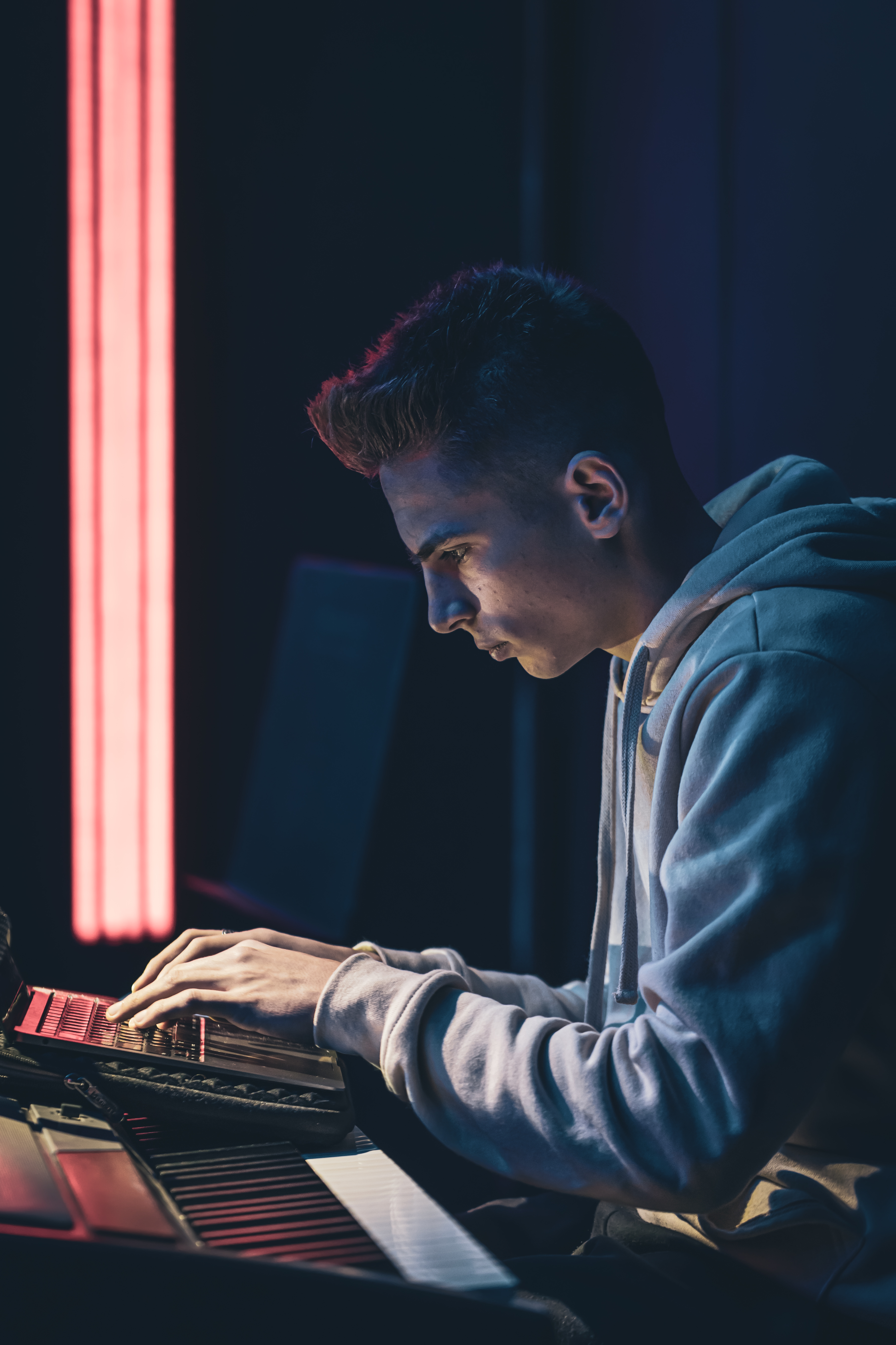 Young man in a dark room at the music keys with a laptop.